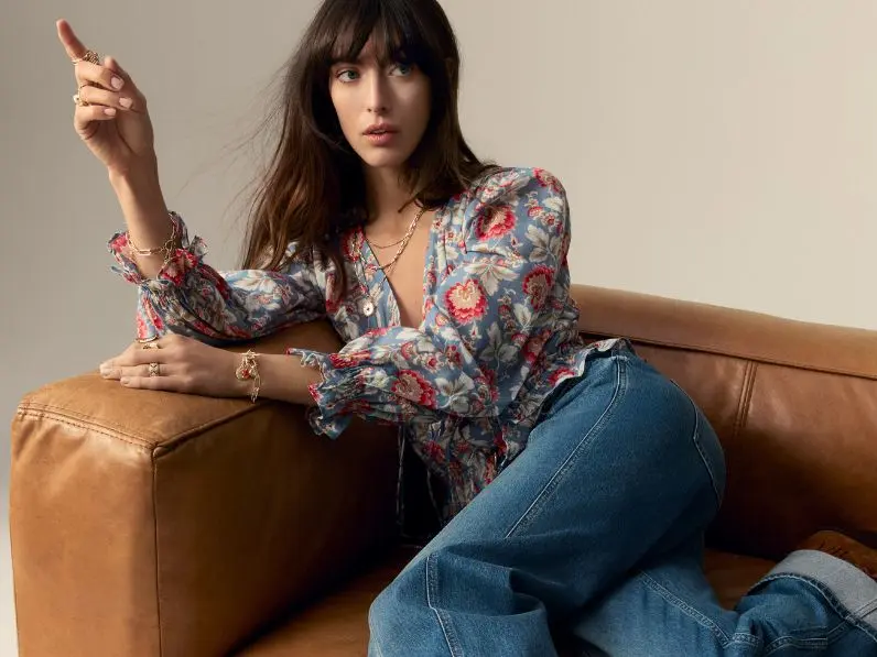 A woman sat on a sofa wearing a Per Una floral blouse with blue loose jeans