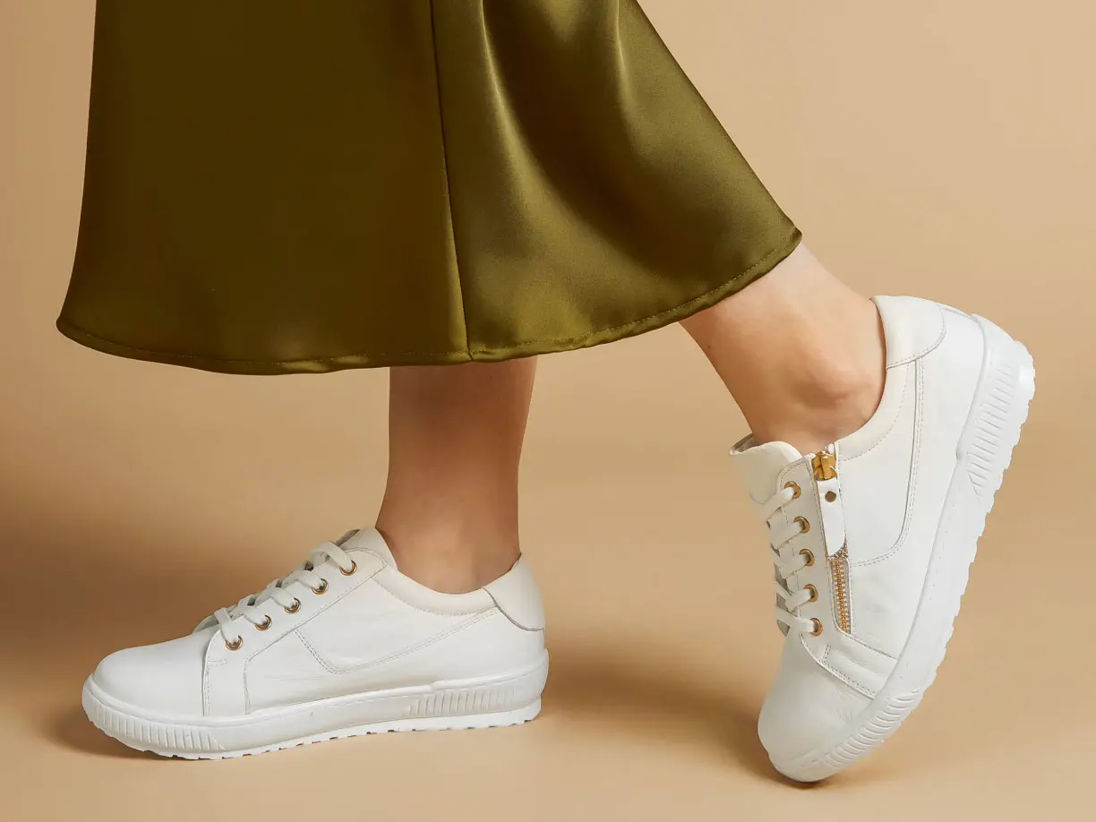 Close-up of woman's legs, wearing green satin skirt and a pair of white trainers with gold zip detail