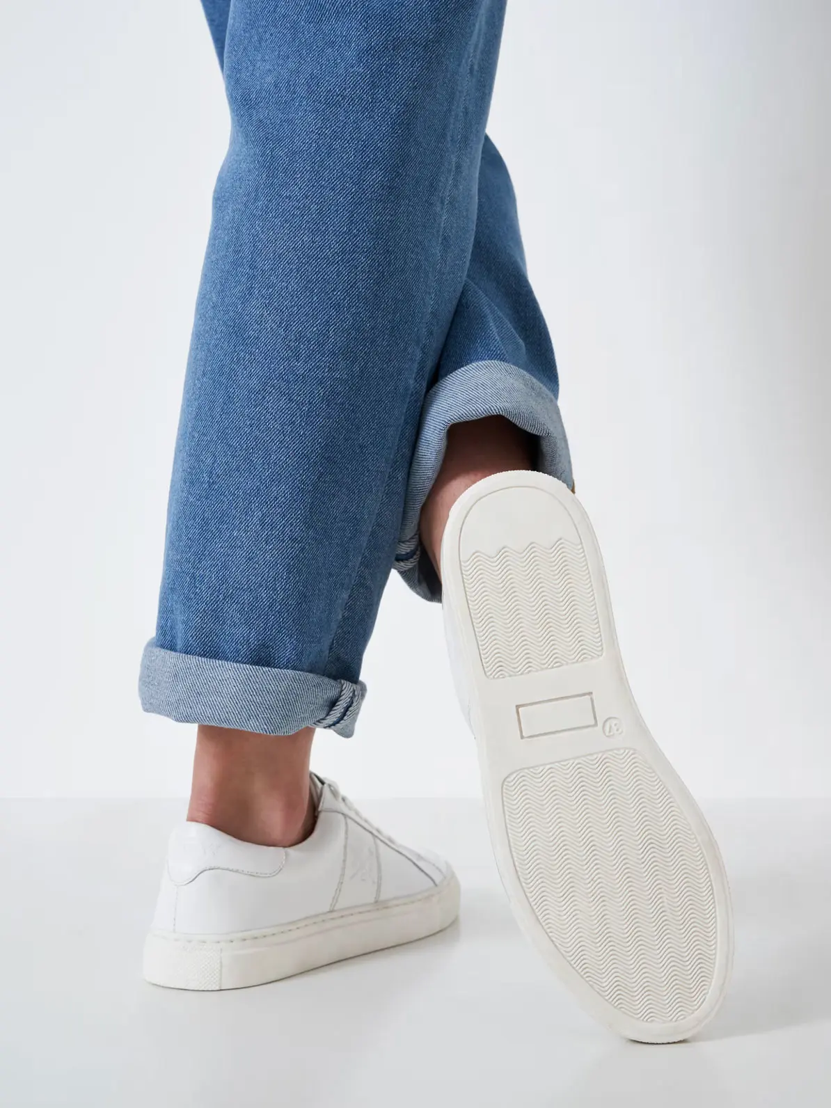 Close up of woman's legs, wearing blue cuffed jeans and white trainers 