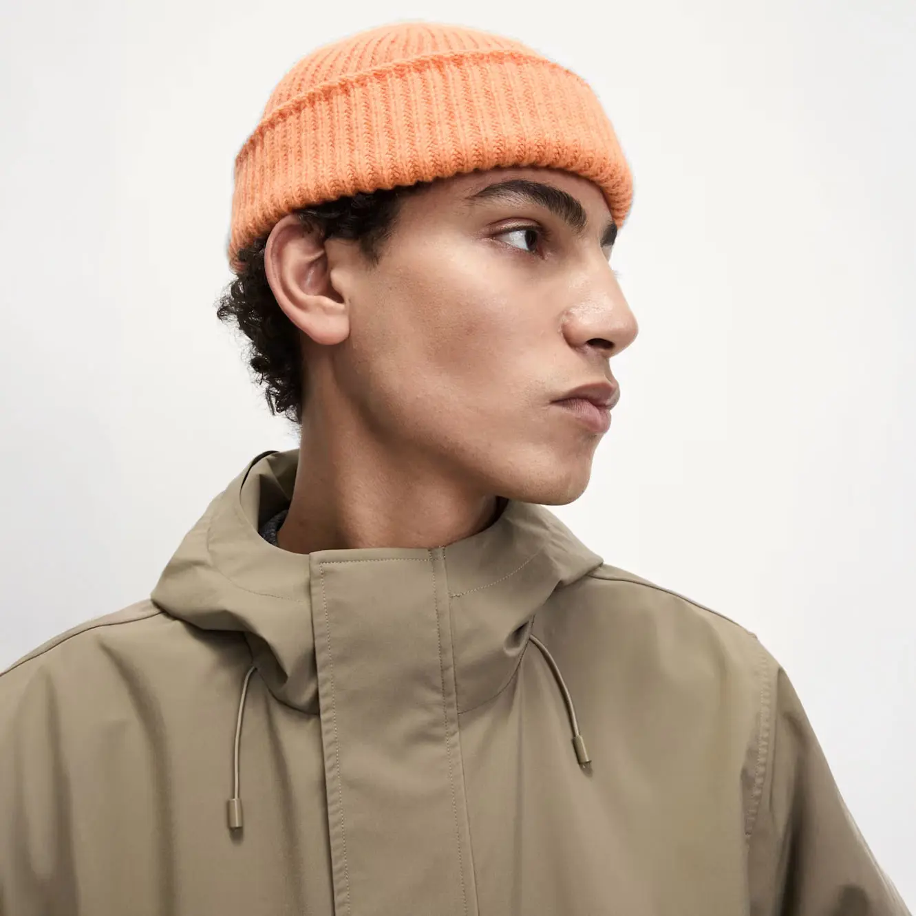 Man wearing a orange beanie with a green raincoat.