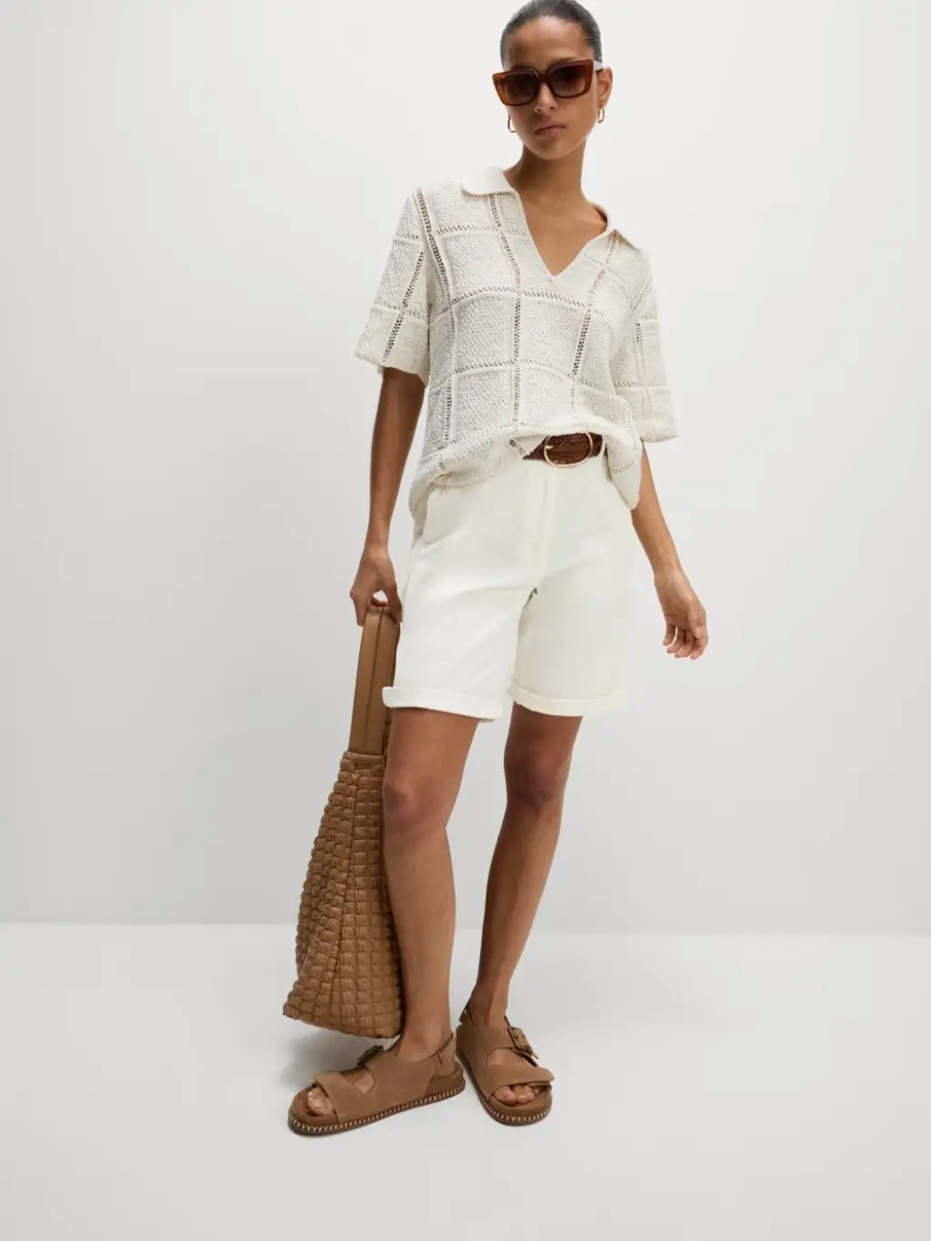 A woman wears an all white outfit with brown suede bag and brown suede sandals