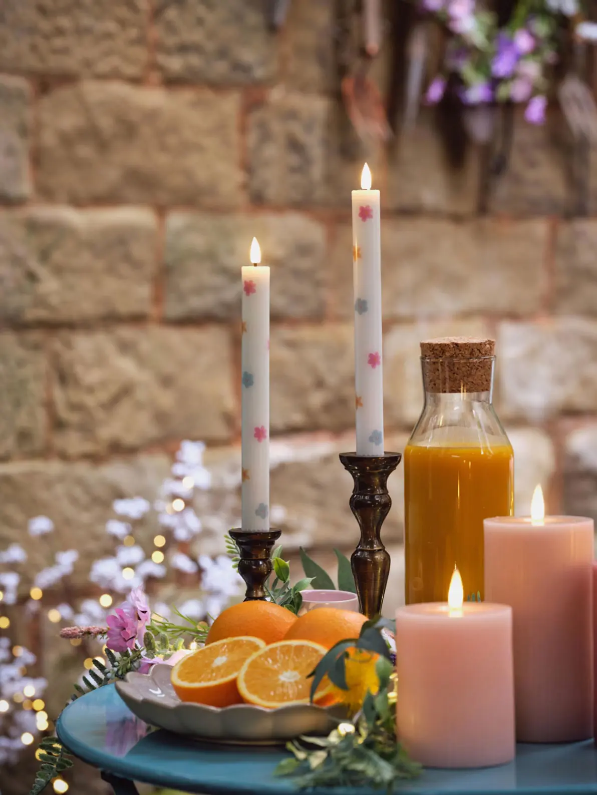 Two lit candlesticks with floral details, bowl of oranges and pink pillar candles 