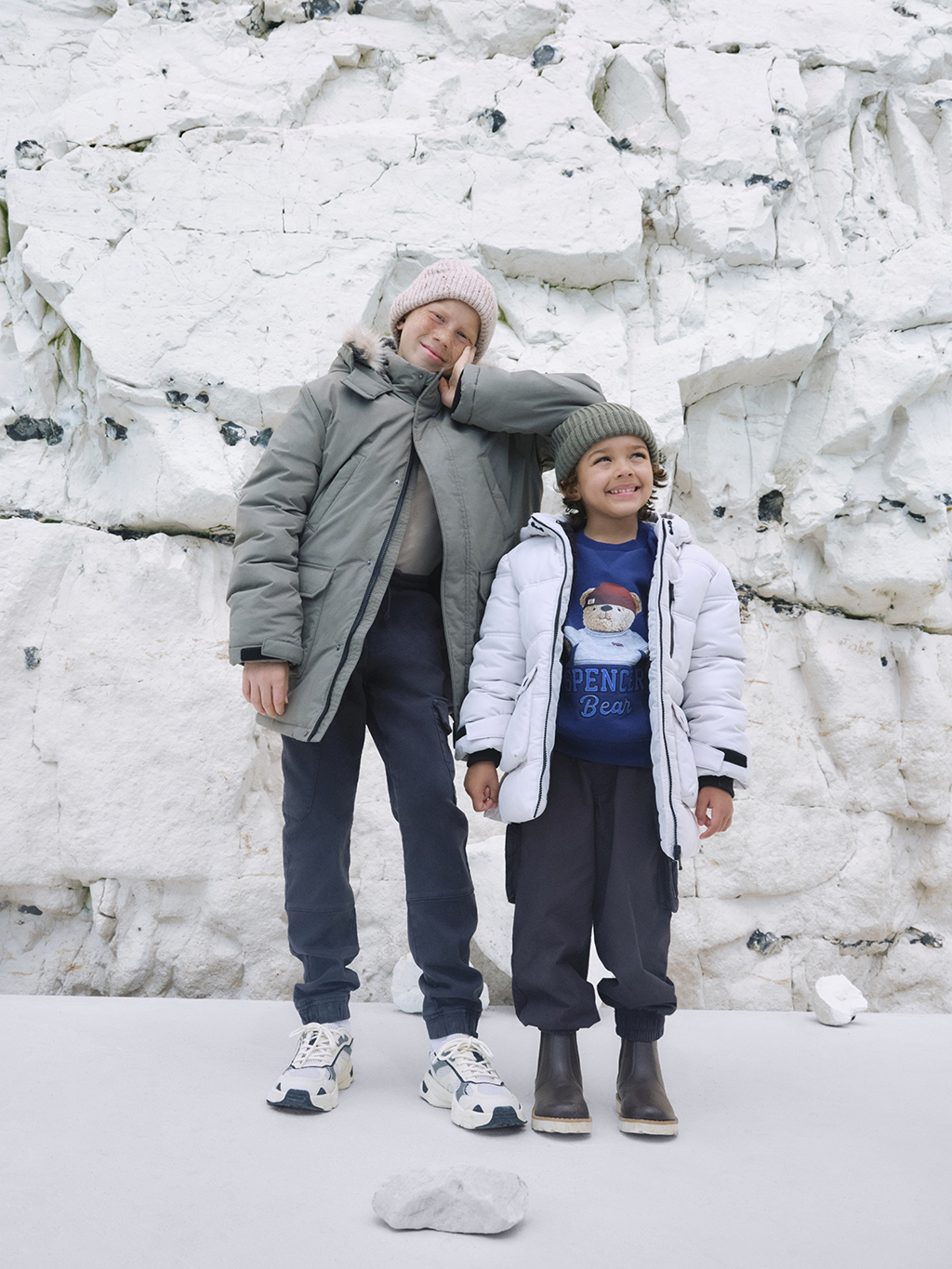 Boys wearing padded raincoats by cliffs at the beach