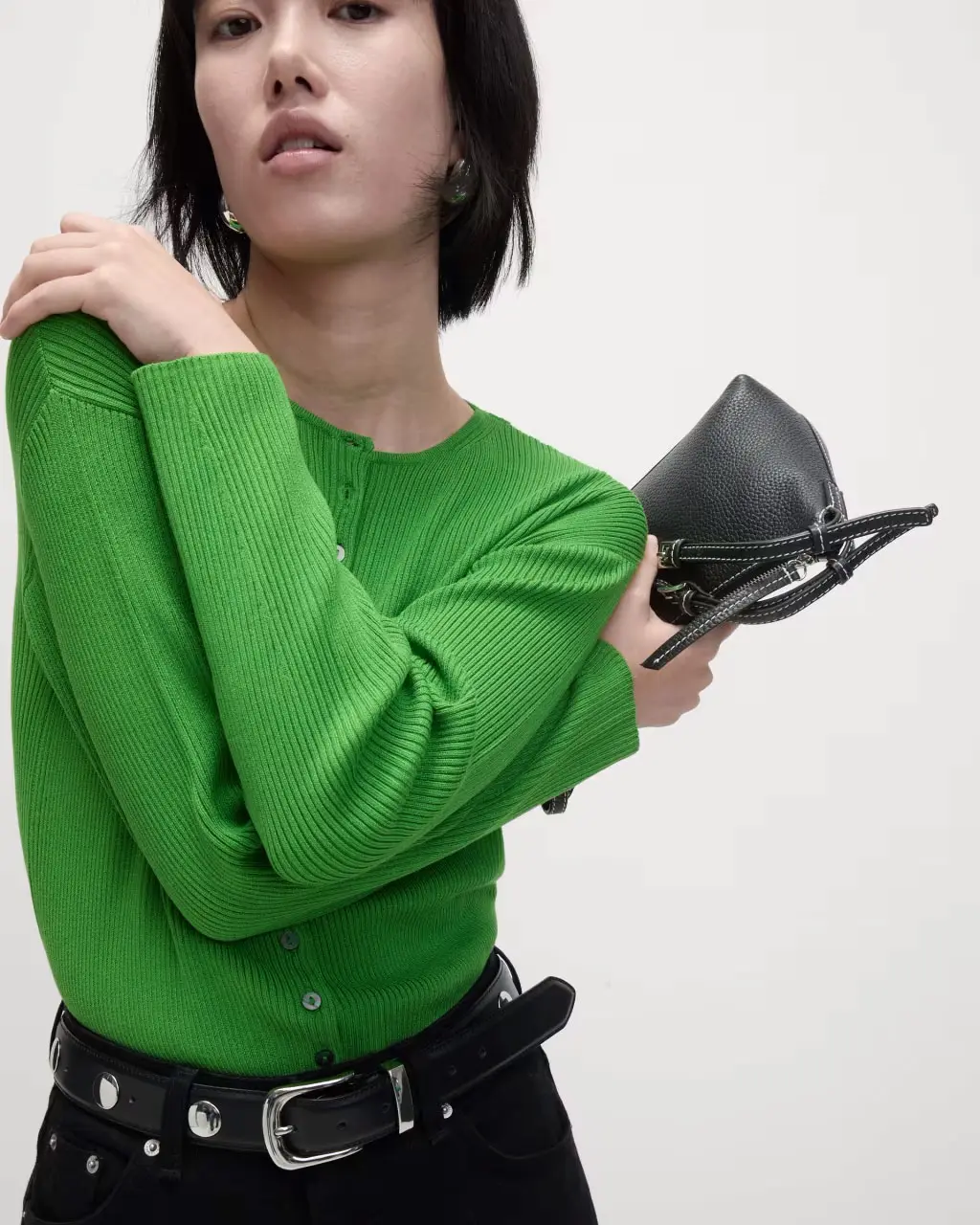 Woman wearing a green cardigan with black jeans, a studded black belt and a black bag.