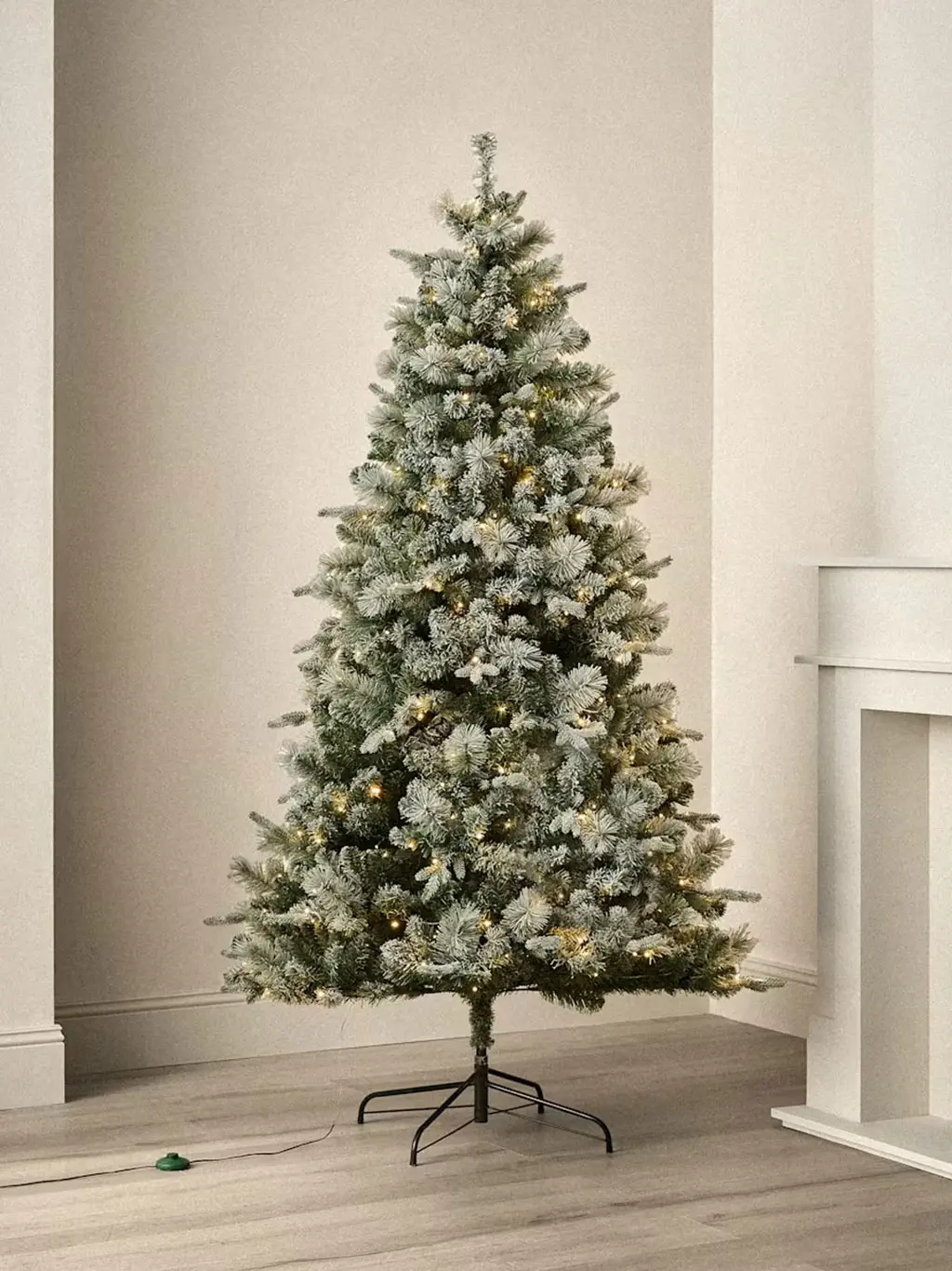 Frosted artificial Christmas tree with warm white lights and metal stand.