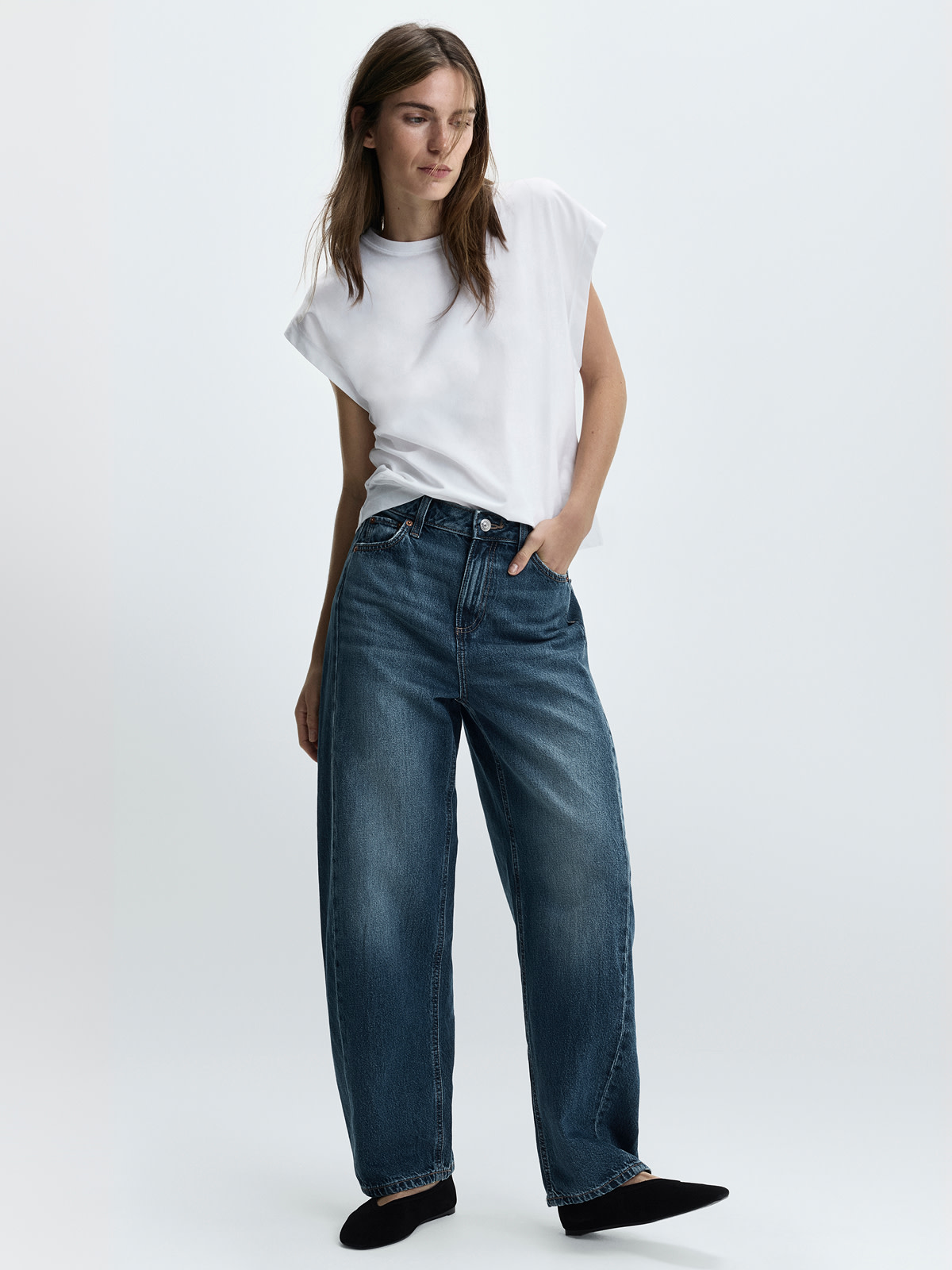 Woman wearing dark barrel jeans and white top