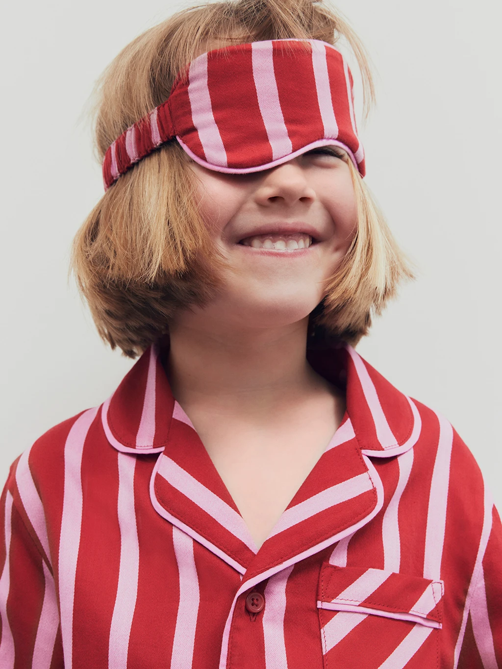 Girl wearing pink and red striped sleep mask and matching pyjama set