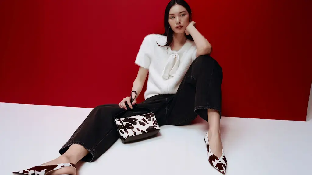 Woman wearing a white bow-detail cardigan with black jeans, cow-print heels and a cow-print bag