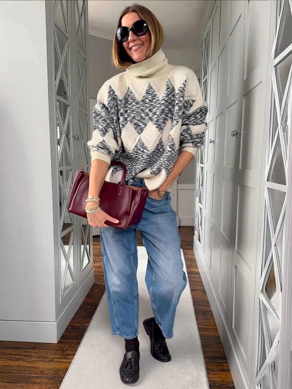 Hayley Karseras wearing a cream argyle jumper with blue jeans, black sunglasses and a burgundy bag