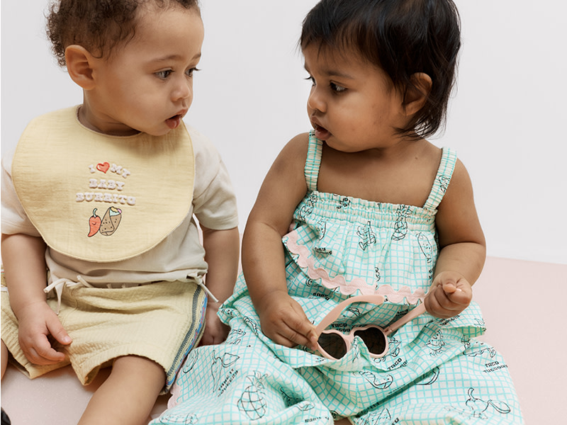 Two babies wearing outfits and bibs with taco graphics