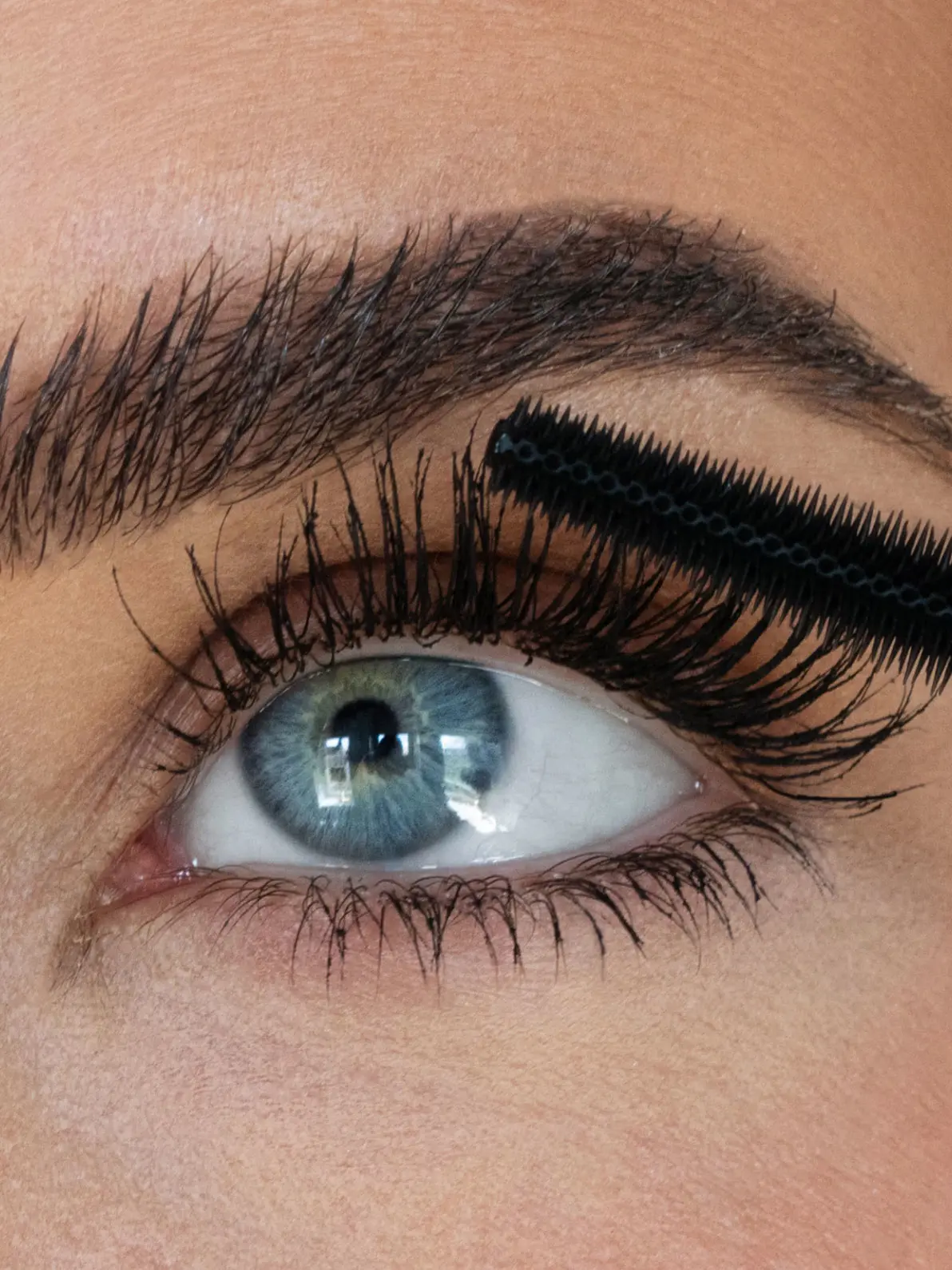 Woman with blue eyes applying black mascara