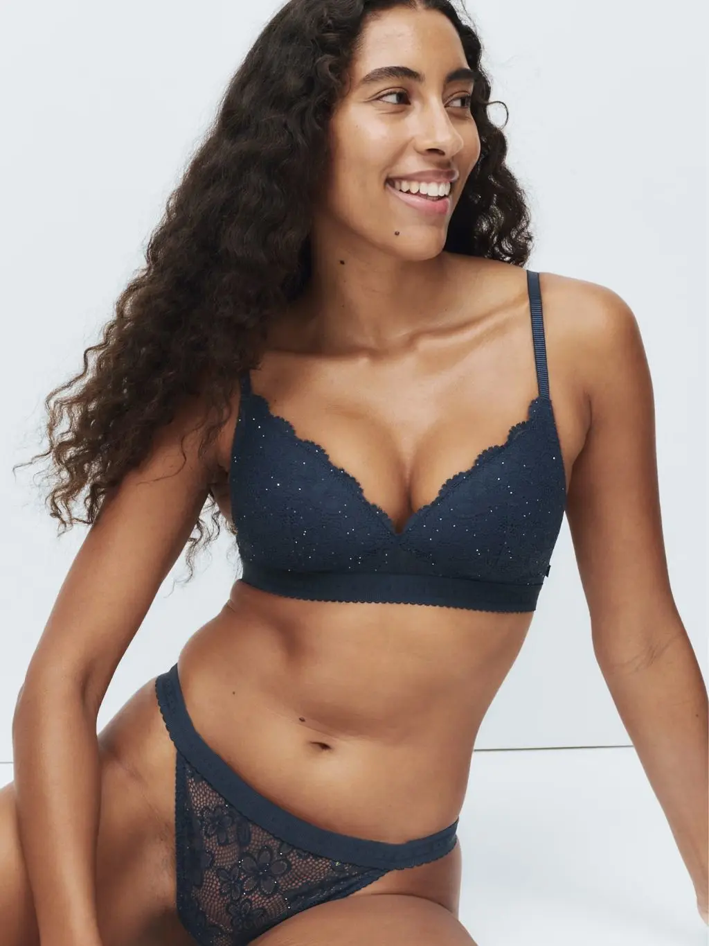 A woman sits on the floor wearing a dark blue plunge non-wire bra and matching knickers