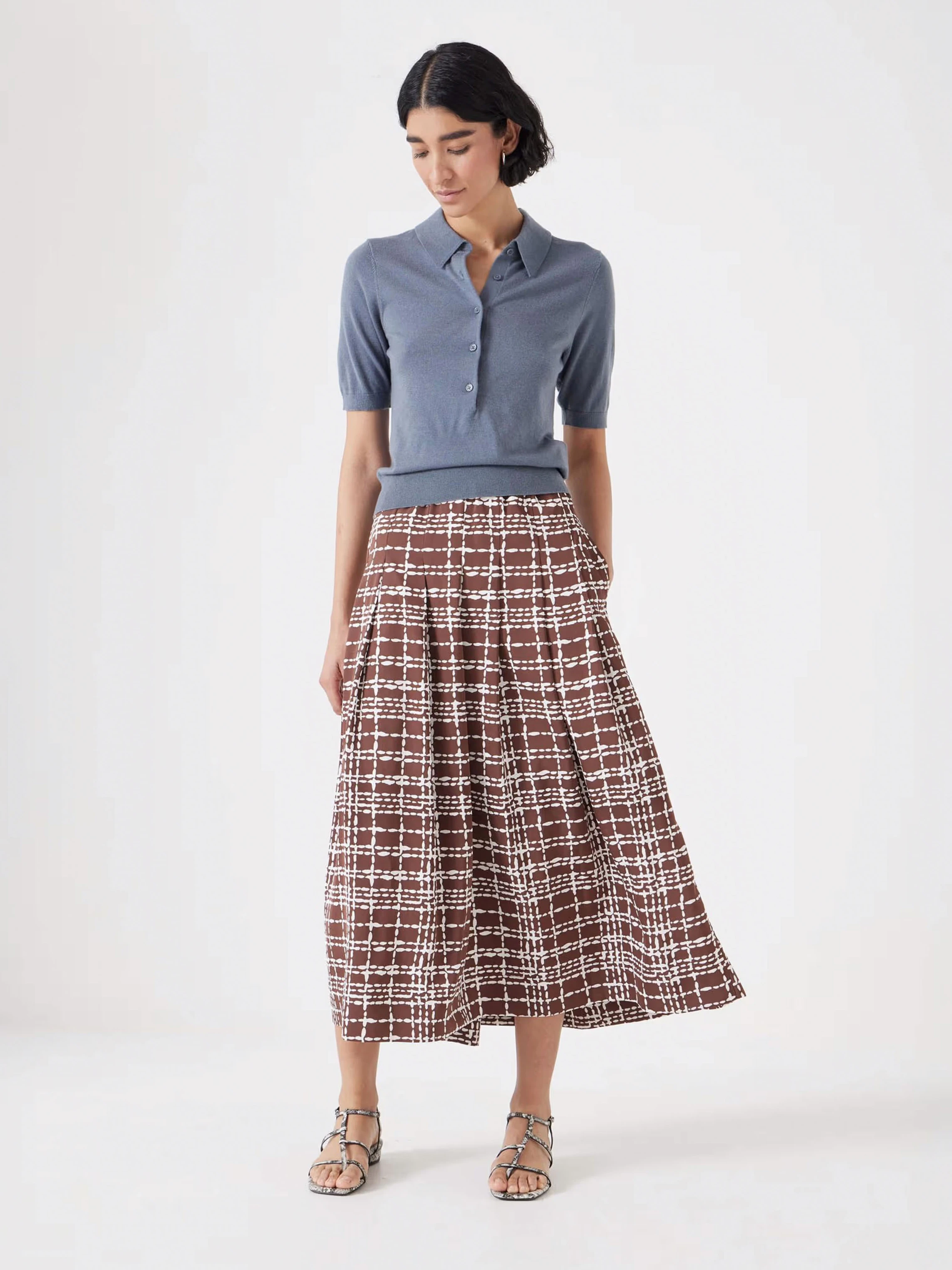 Woman wearing grey polo sweater with a brown checked pleated midi skirt by Hush