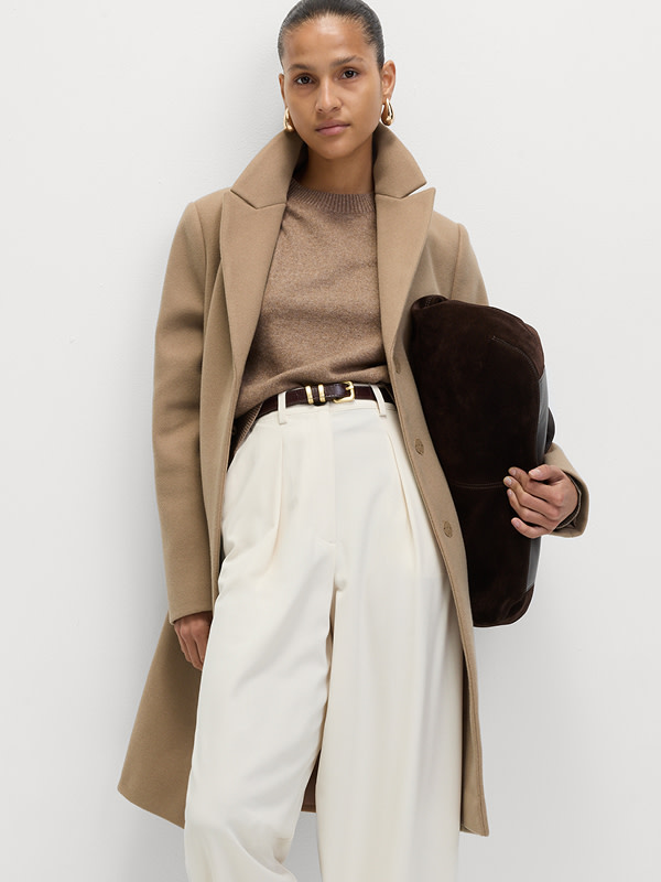 Woman wearing a camel coat, camel jumper and white high-waisted trousers