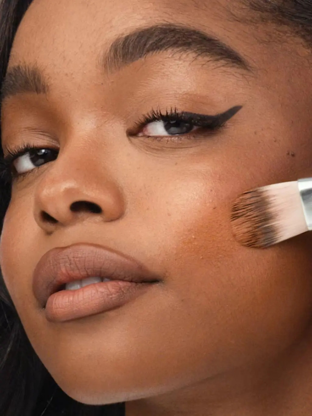 A close up shot of a woman applying foundation with a brush to her skin