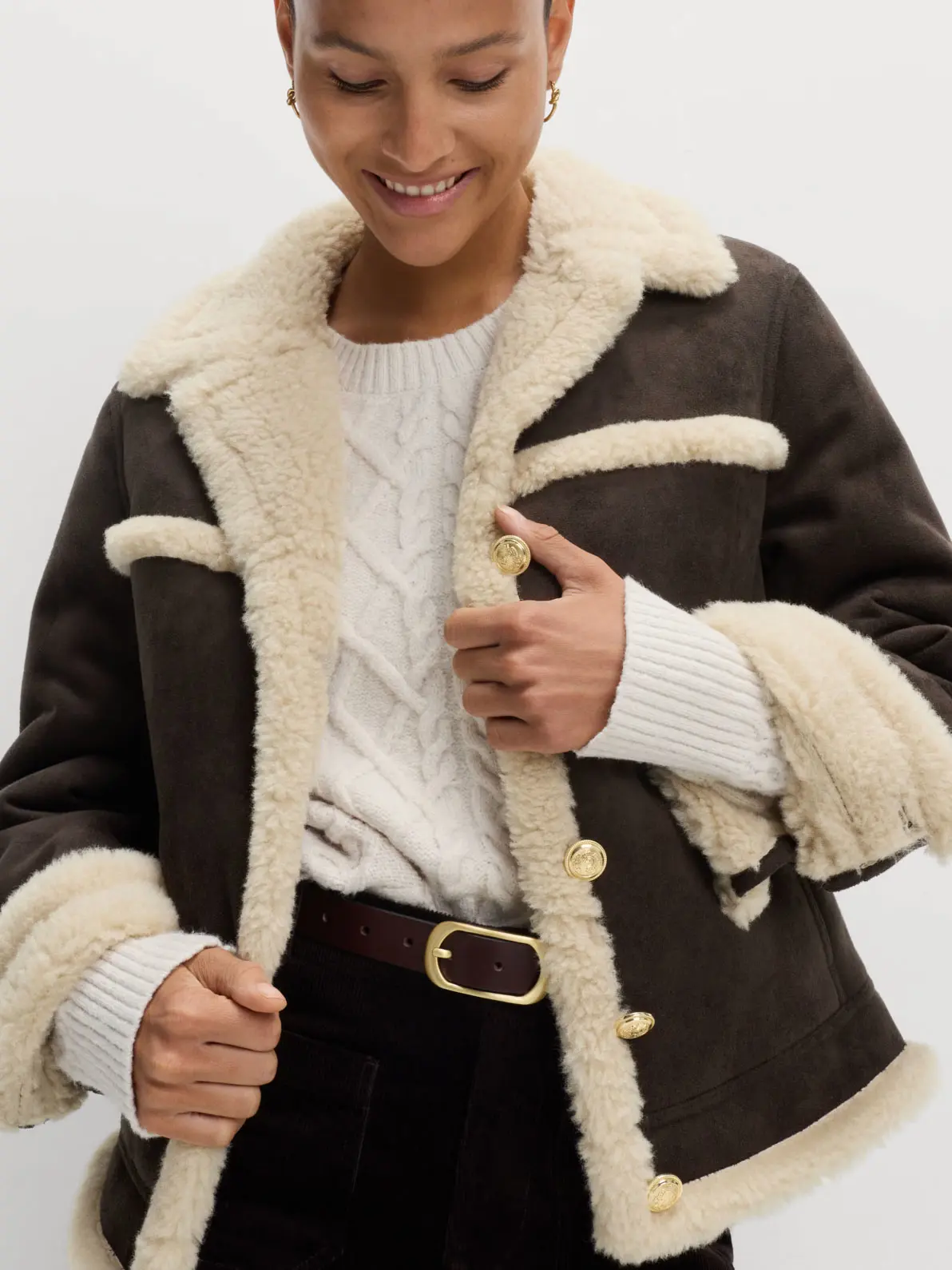 Woman wearing brown suede aviator jacket with faux-fur shearling trim, plus white jumper tucked into black jeans, complete with a brown belt