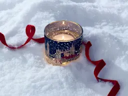 A light up M&S Christmas candle on the snow, surrounded by red ribbon