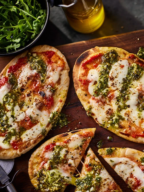 Pitta pizzas with drizzle of green pesto on wooden board