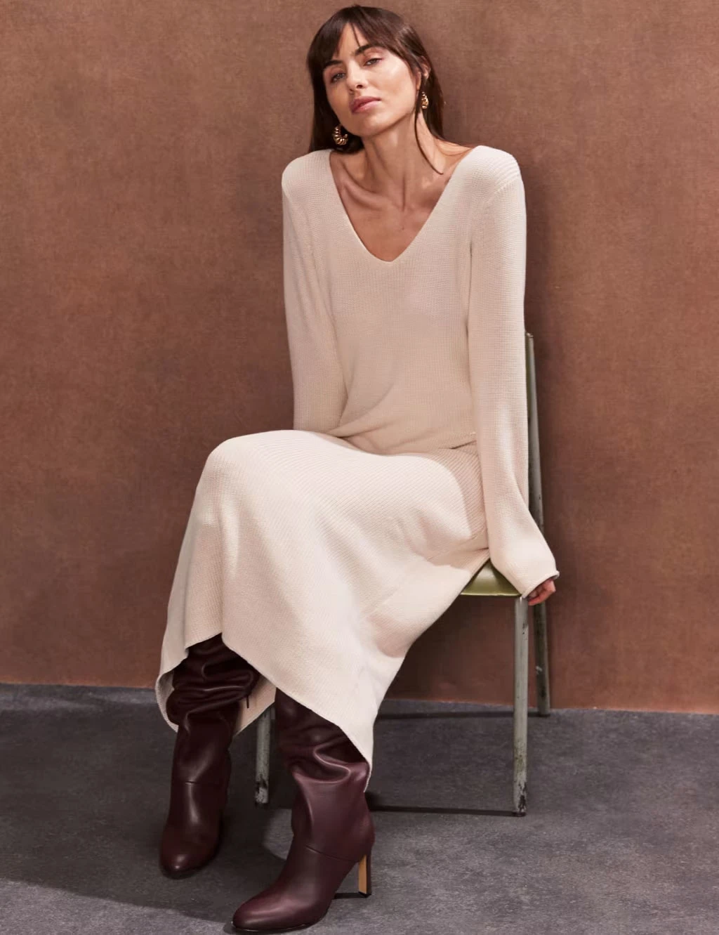 Woman wearing cream V-neck sweater dress and burgundy knee-high boots