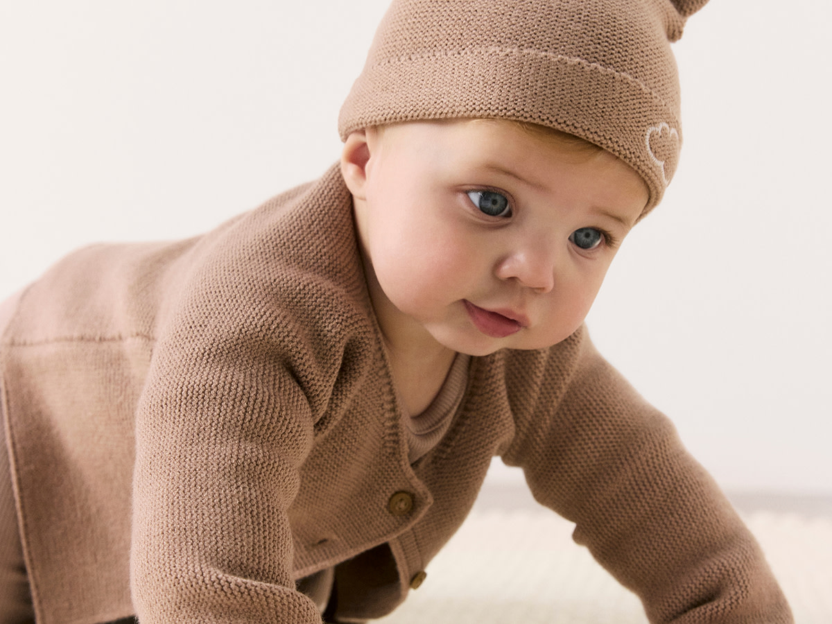 Baby wearing light brown hat and cardigan