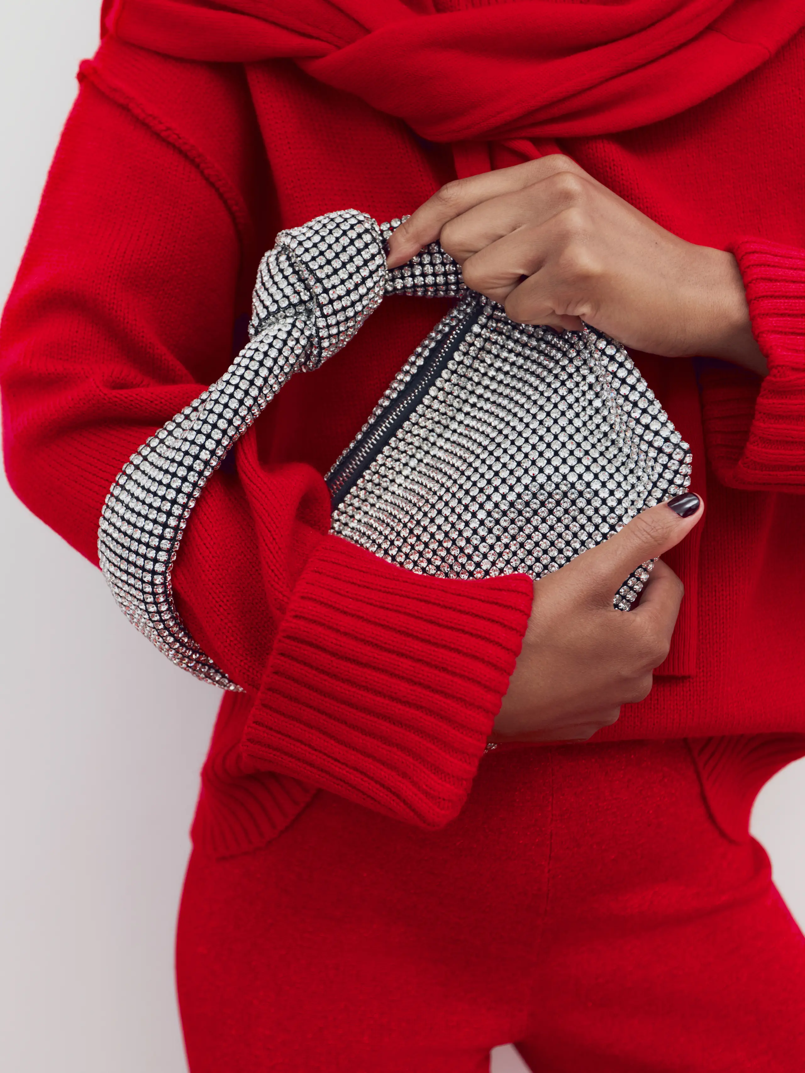 Image of woman wearing red knitted jumper and trousers, holding metallic shoulder bag