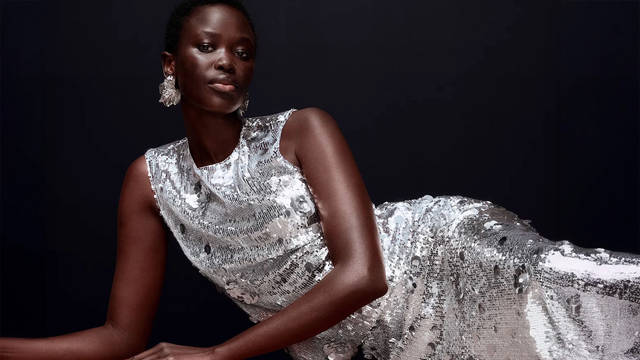 Woman wearing silver earrings and a silver sequinned sleeveless dress