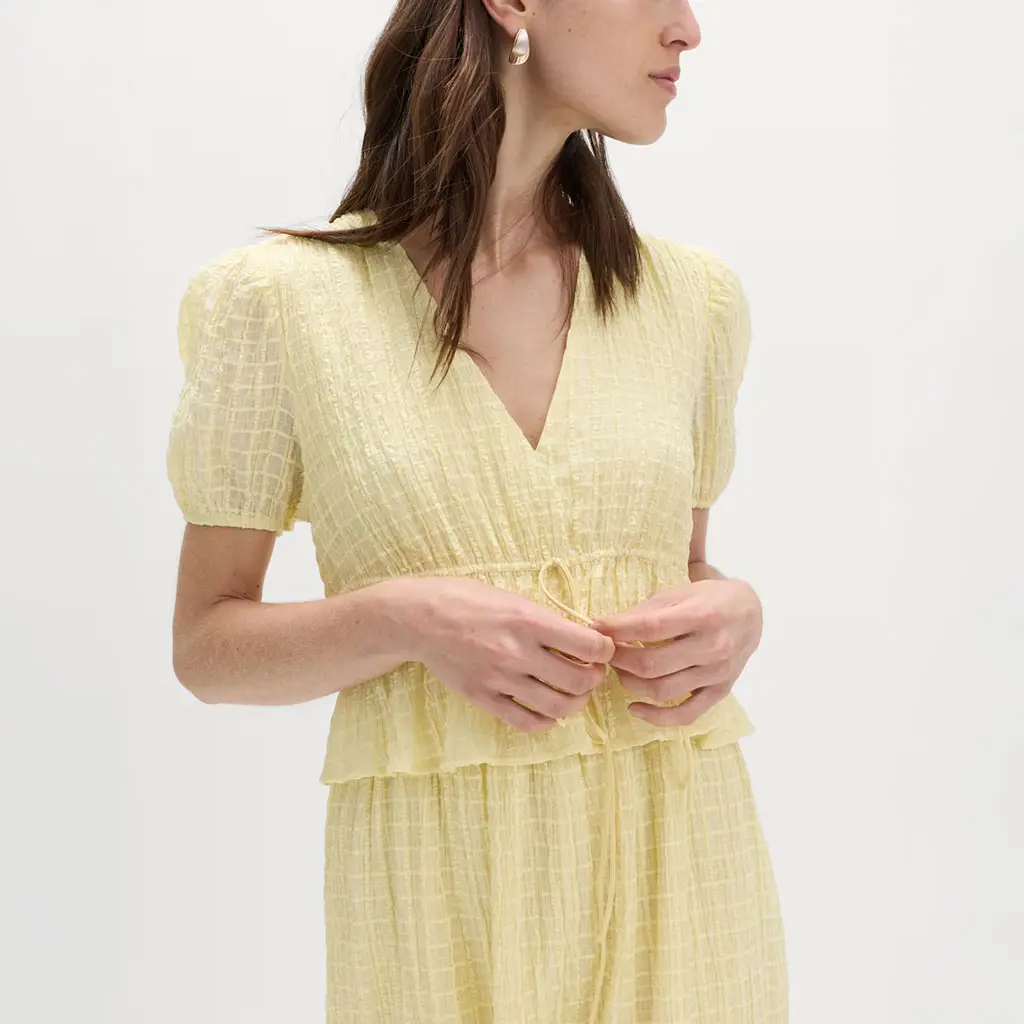 Woman wearing a yellow seersucker dress with gold jewellery