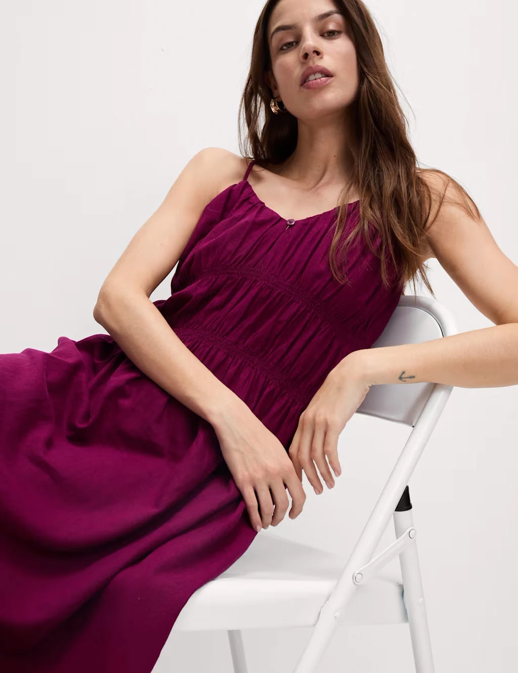 A woman in a raspberry sleeveless dress sitting on a white chair