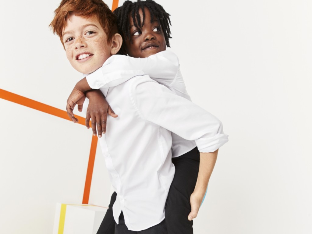 Two boys wearing white long-sleeved shirts and black trousers. Shop boys’ uniform