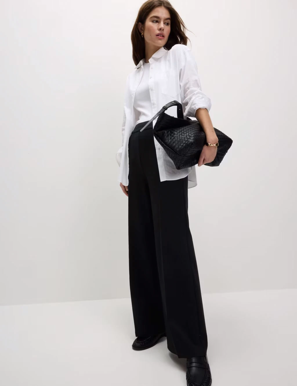 Woman wearing a white vest with a white shirt, black wide-leg trousers, black loafers and a black tote bag.