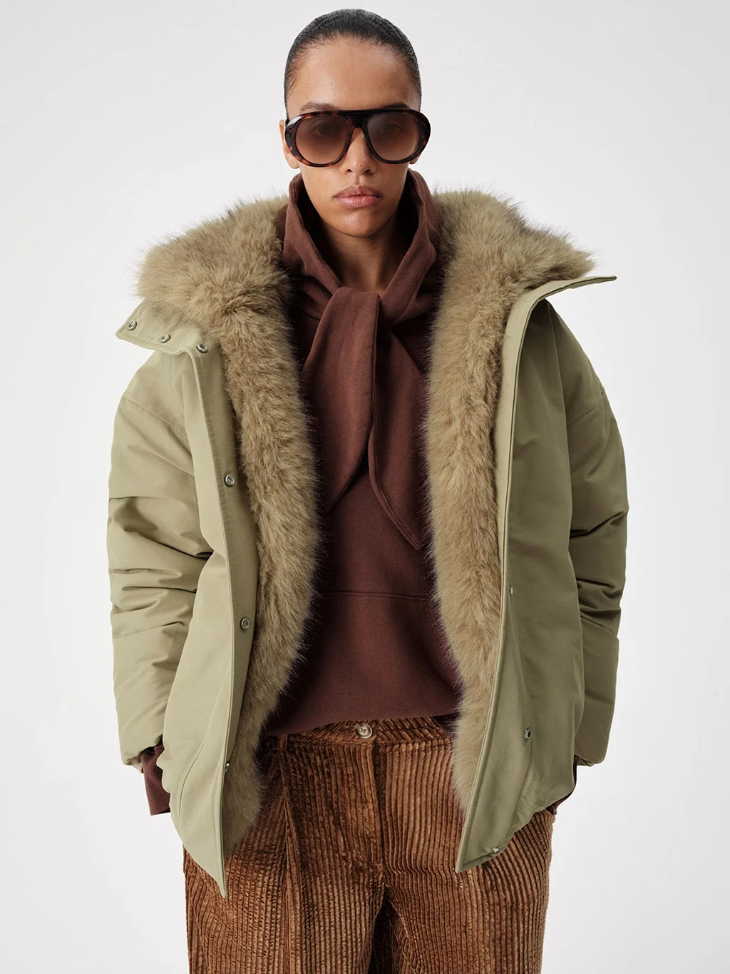 Model wearing a green parka coat with a faux fur lining and brown hoodie.