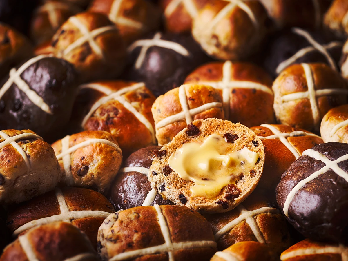 A selection of hot cross buns in flavours like classic and chocolatey and a toasted hot cross bun with butter.