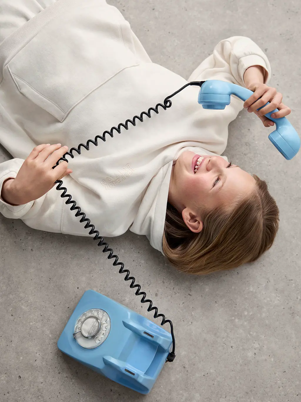 Girl wearing an ecru hoodie and joggers, holding a vintage blue telephone