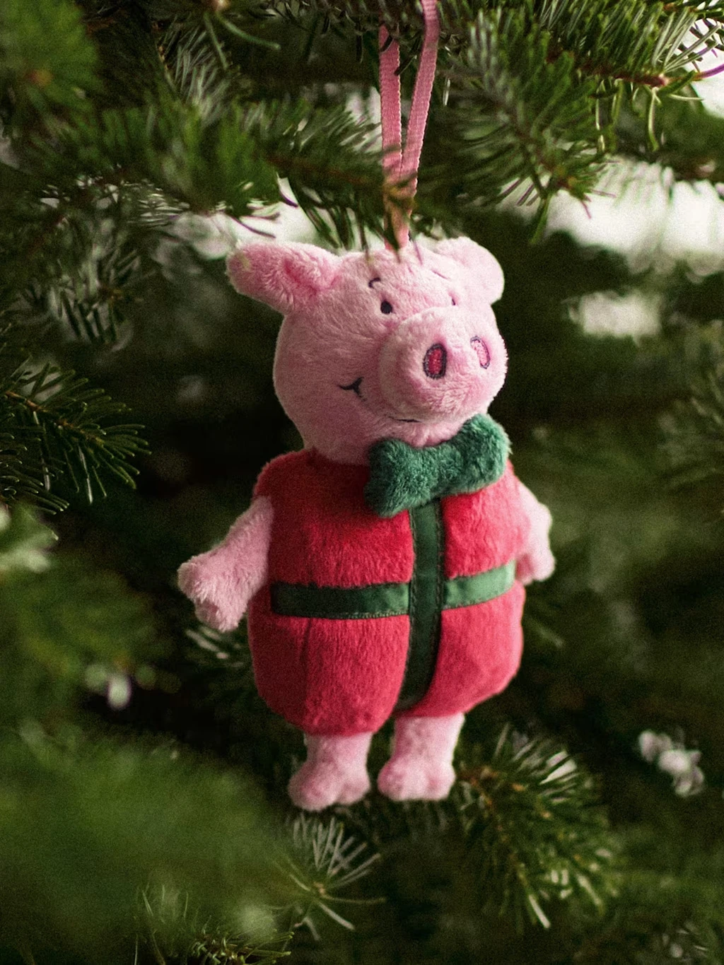 Percy Pig decoration hanging from a Christmas tree and dressed as a red present.