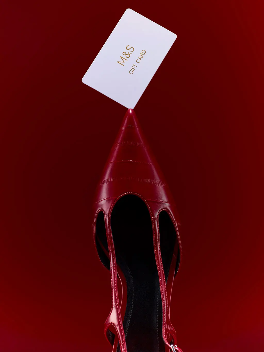 Red pointed toe shoe with an M&S gift card balancing on top.
