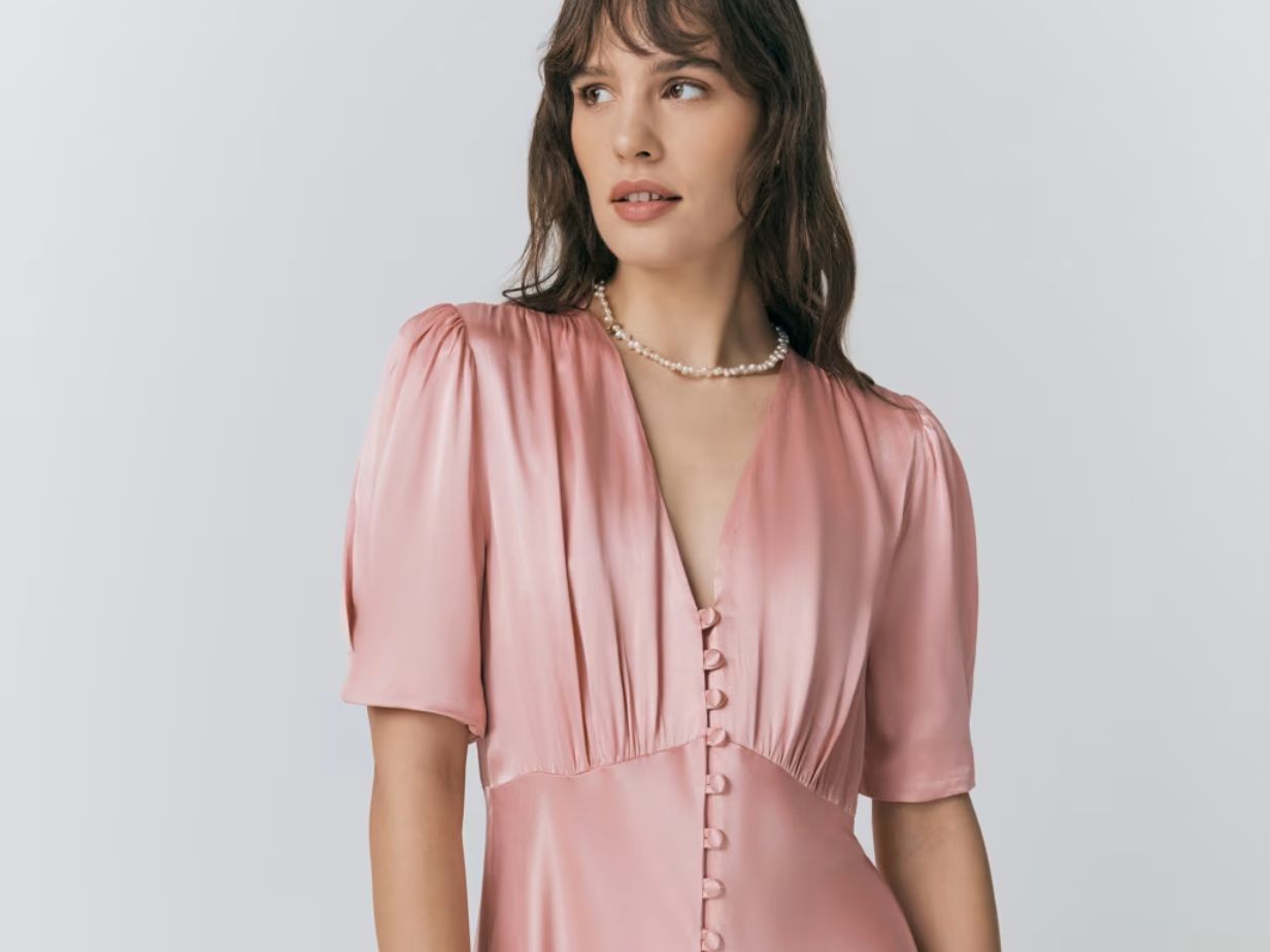 A model, looking away from the camera, wears a pink satin dress