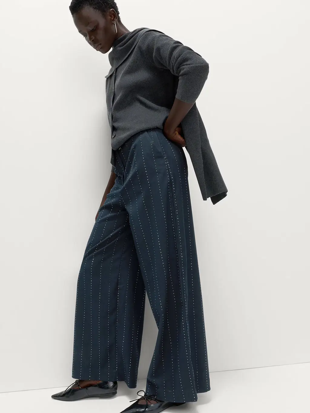 Woman wearing a grey sweater with navy pinstriped trousers, pointed pumps and silver jewellery