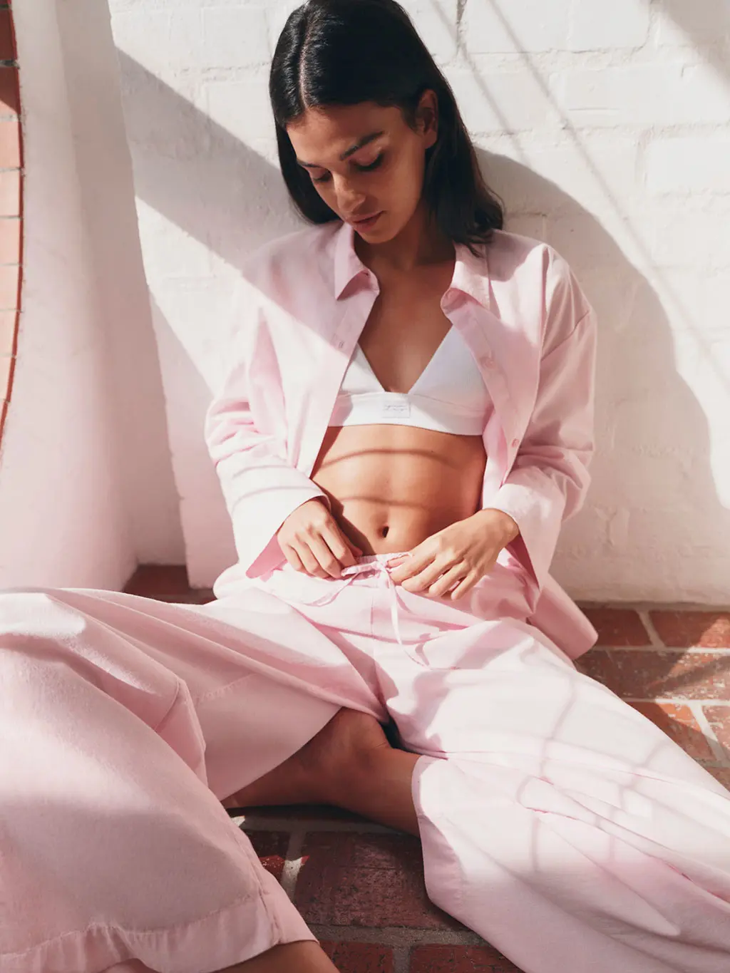 Woman wearing pink shirt and trouser pyjamas with a white bralette