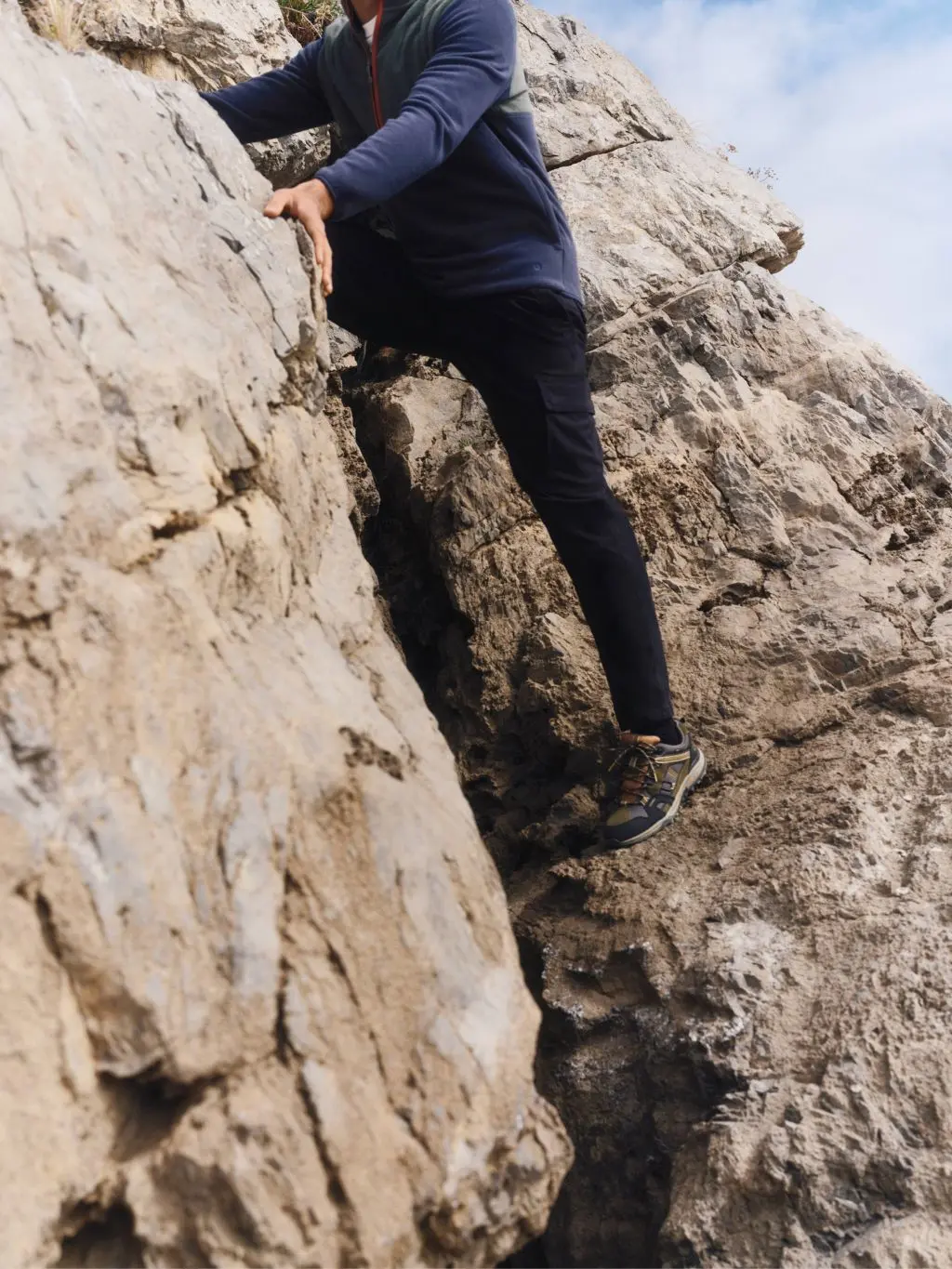 A close up of a man climbing up a rock wearing trouseres and hiking trainers