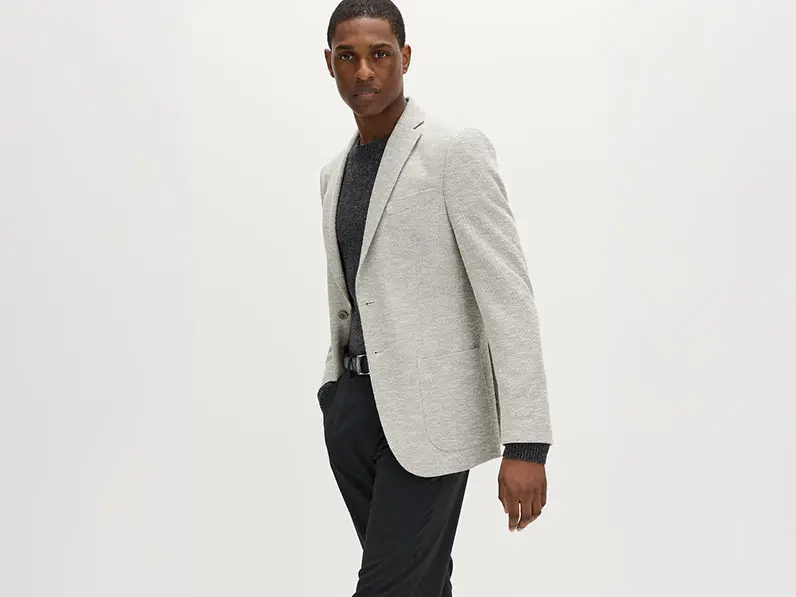 Man wearing a black jumper, black trousers and a light-grey blazer