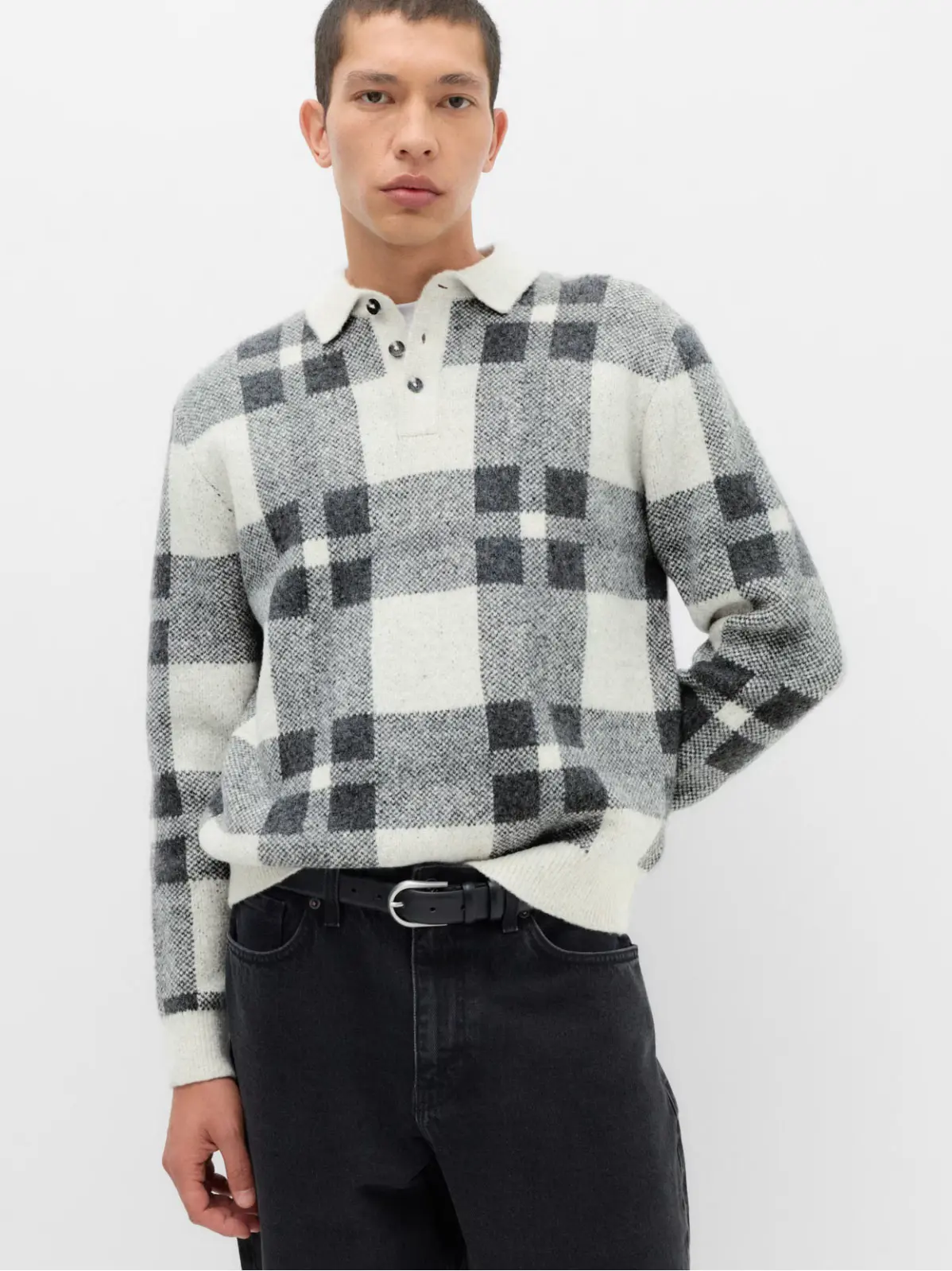 Man wearing grey and white checked polo jumper with dark jeans 