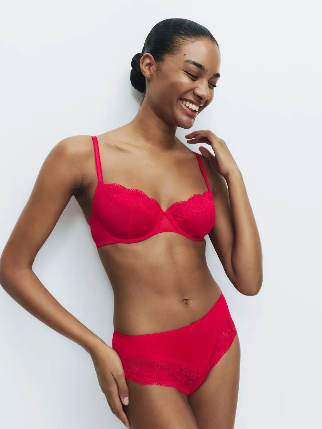A woman wears a matching red bra and pants, smiling off away from the camera