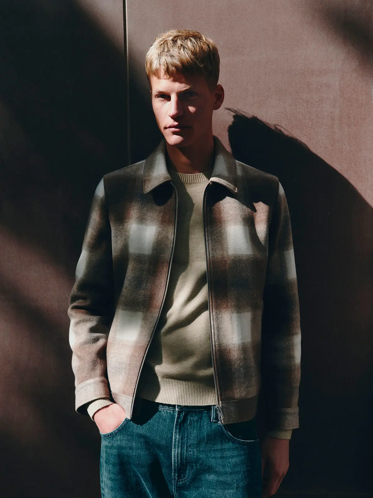 Man wearing checked jacket, a light neutral jumper and blue jeans 