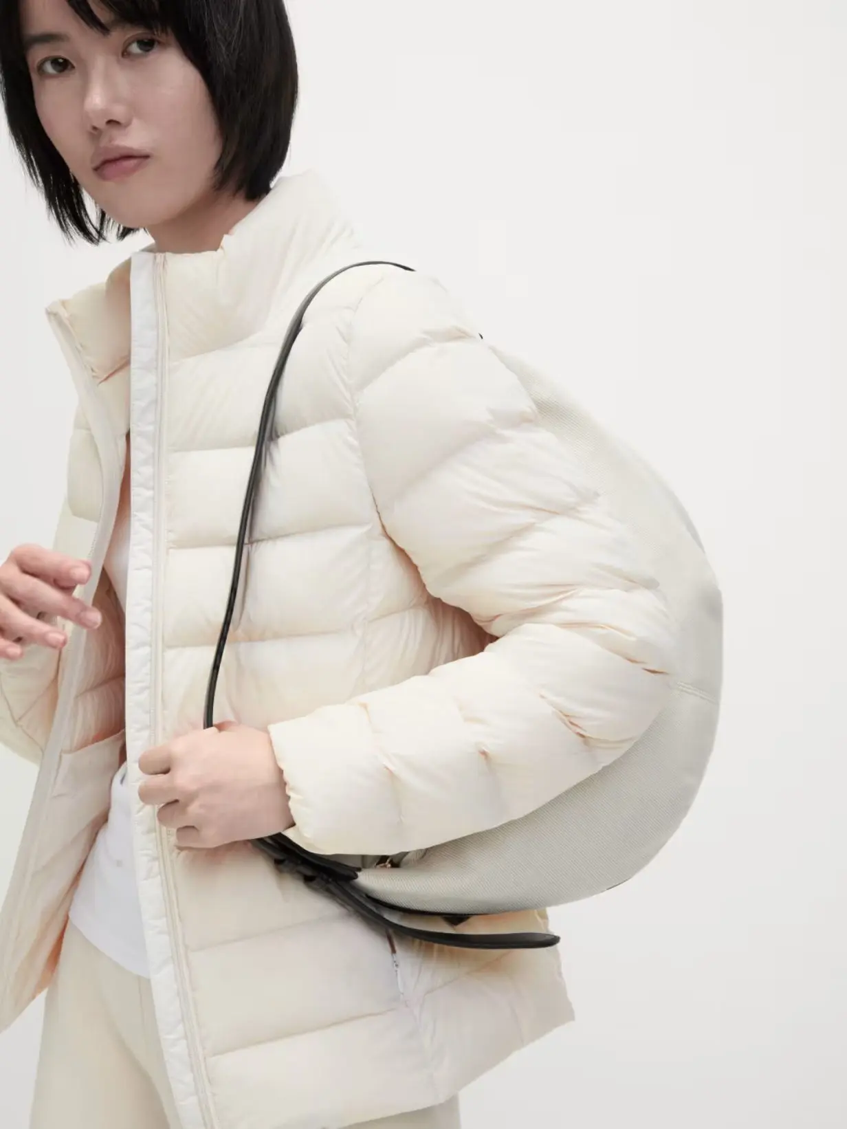 A woman wearing a cream puffer jacket, carrying a cream handbag