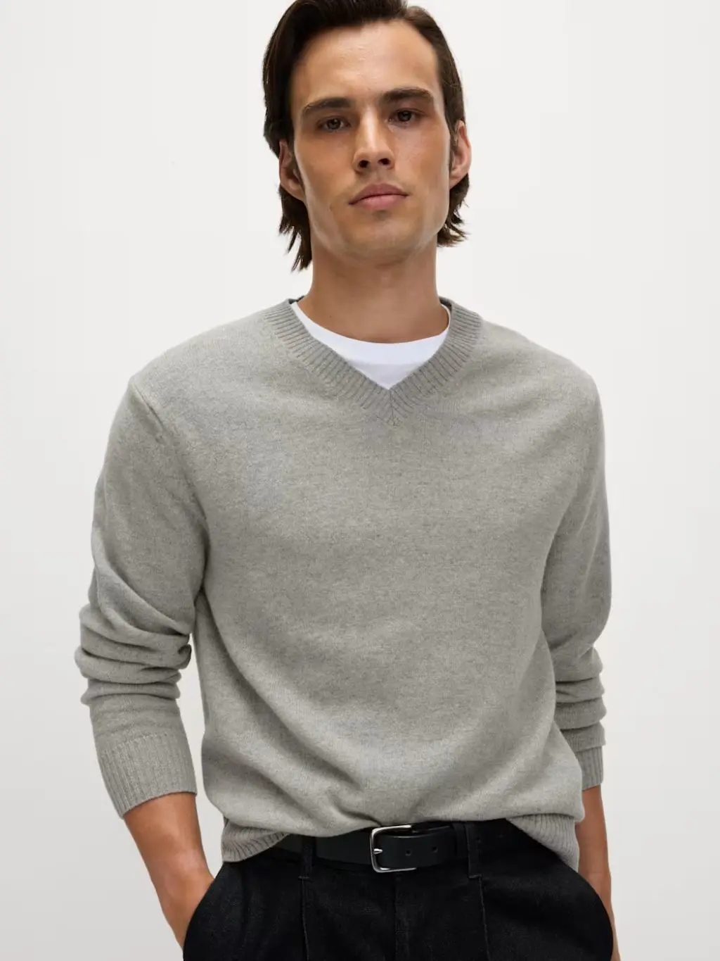 A man wears a grey v-neck jumper with a t-shirt underneath it