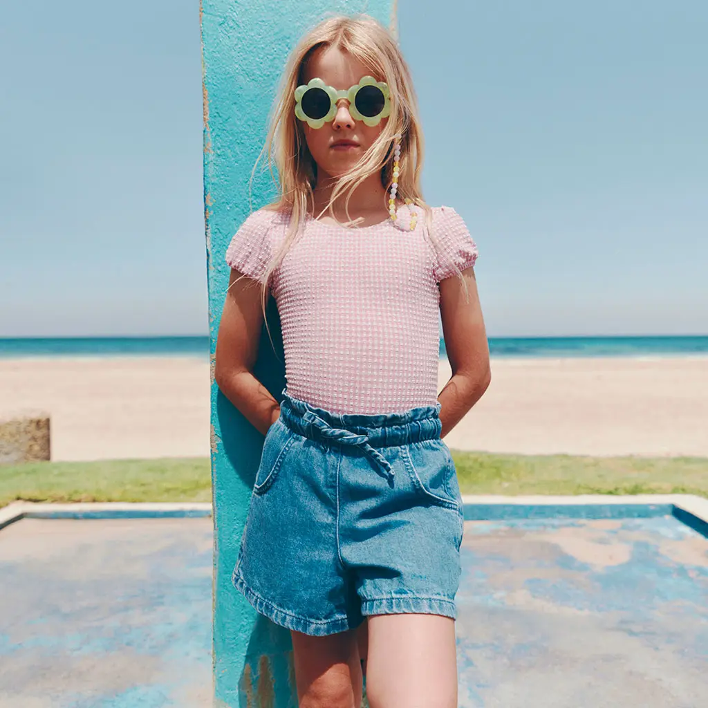 Girl wearing swimming costume with denim shorts and green sunglasses
