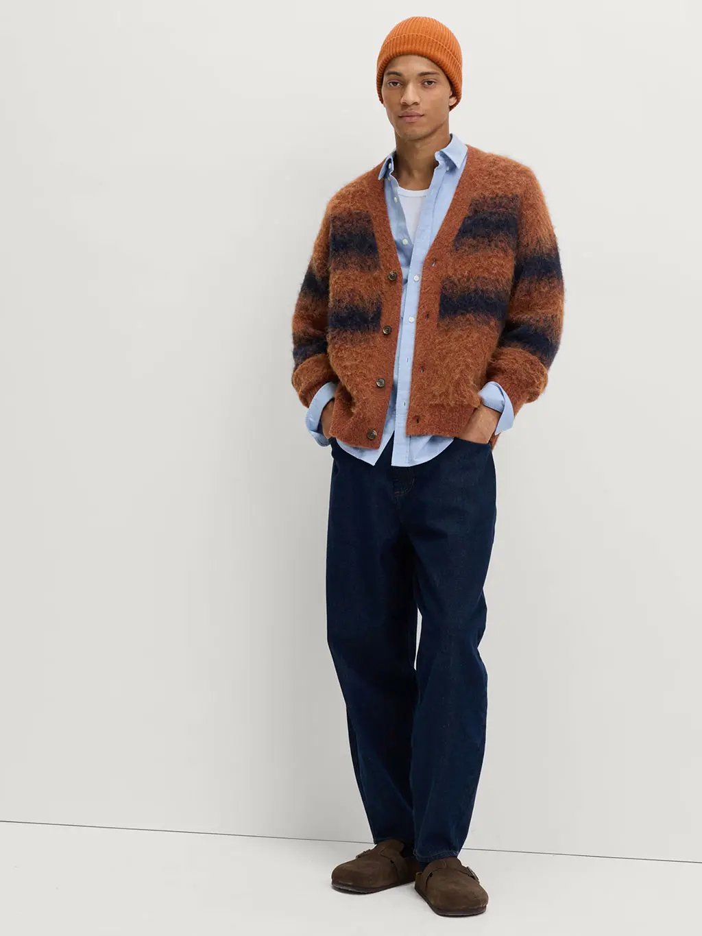 Man wearing striped orange cardigan with a blue shirt and white T-shirt, black trousers, brown shoes and orange beanie