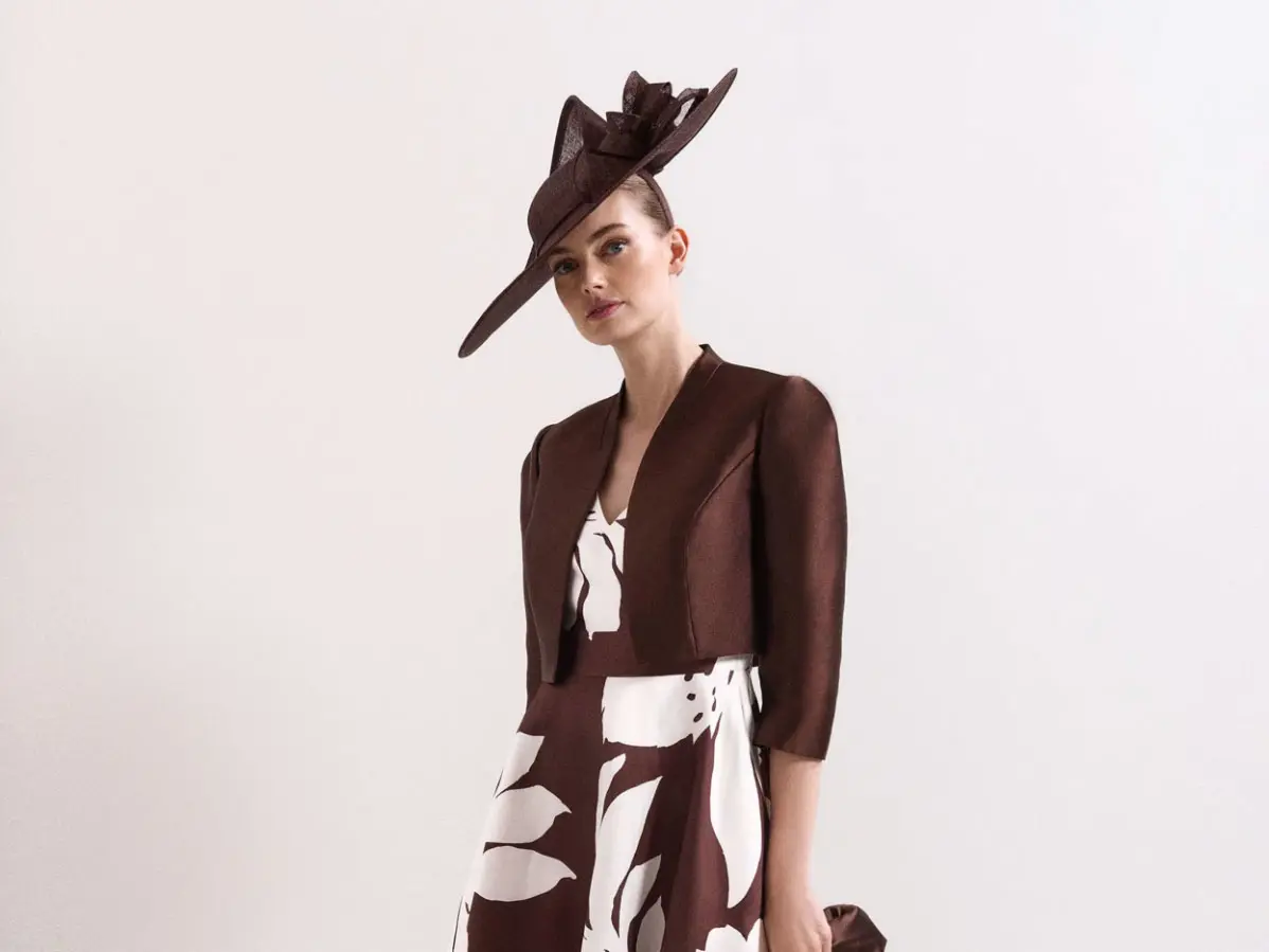 Woman wearing brown and white floral dress with matching blazer and fascinator 