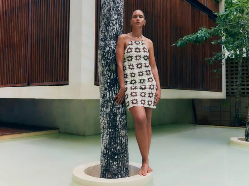 A woman stood next to a tree, wears a crochet dress