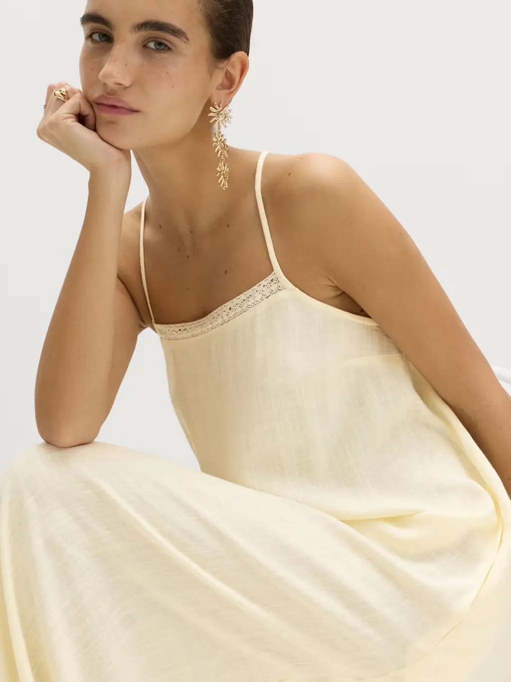 Woman wearing a cream maxi dress with gold drop earrings and stacked rings
